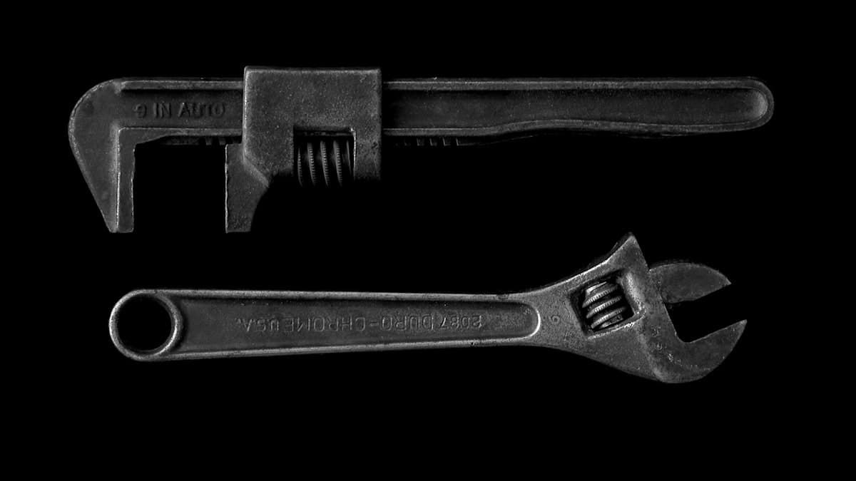 A vintage pipe wrench and adjustable wrench on a black background