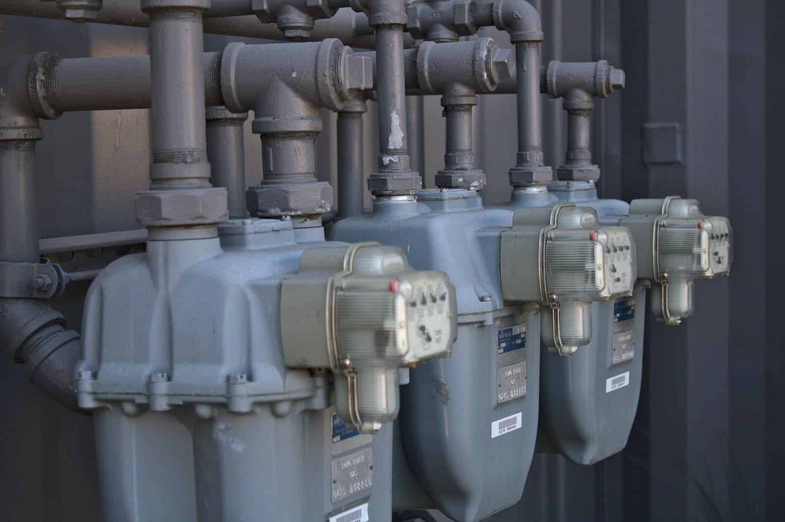 A bank of outdoor utility meters and exposed pipework mounted on a commercial building