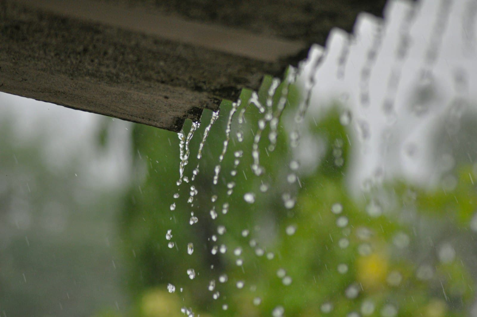 Rainwater streaming off the edge of a roof during a summer downpour