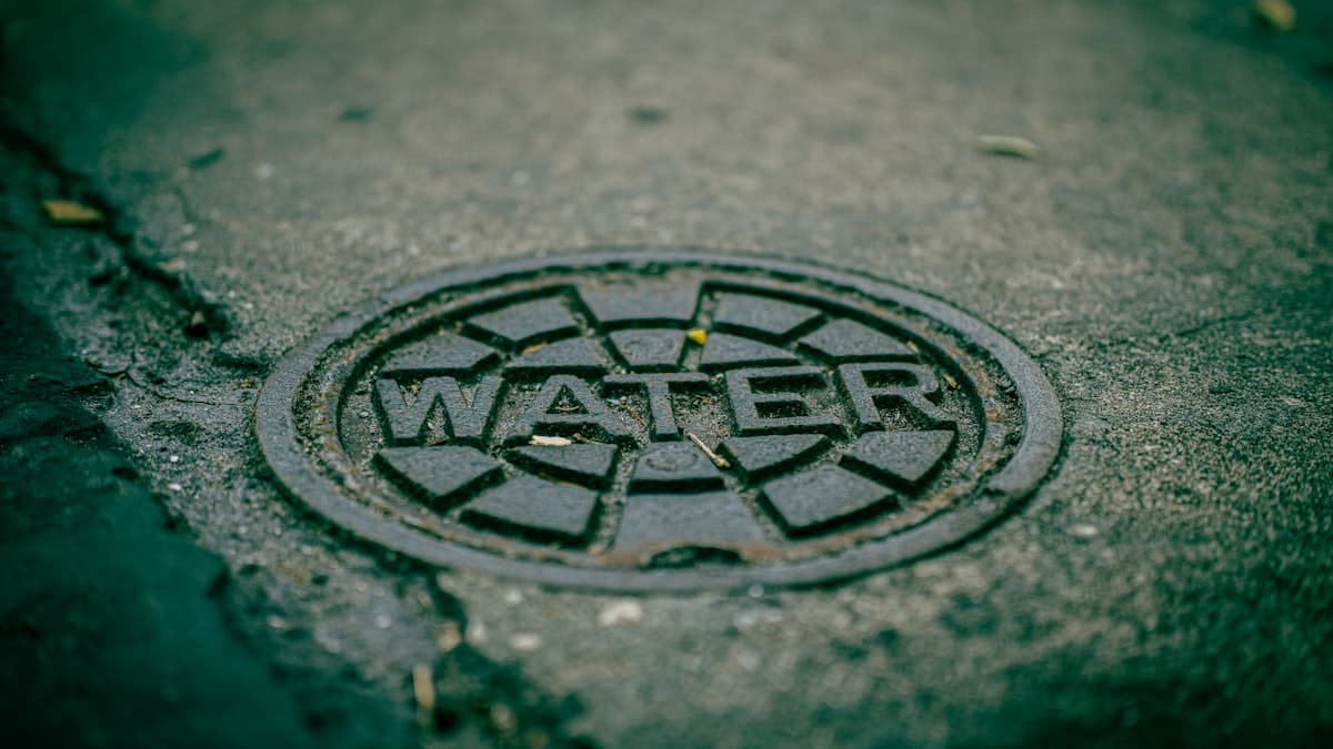 A cast-iron water utility cover set into wet asphalt