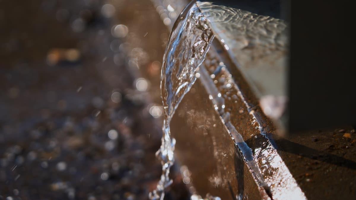 Water gushing from the end of a metal pipe onto wet gravel
