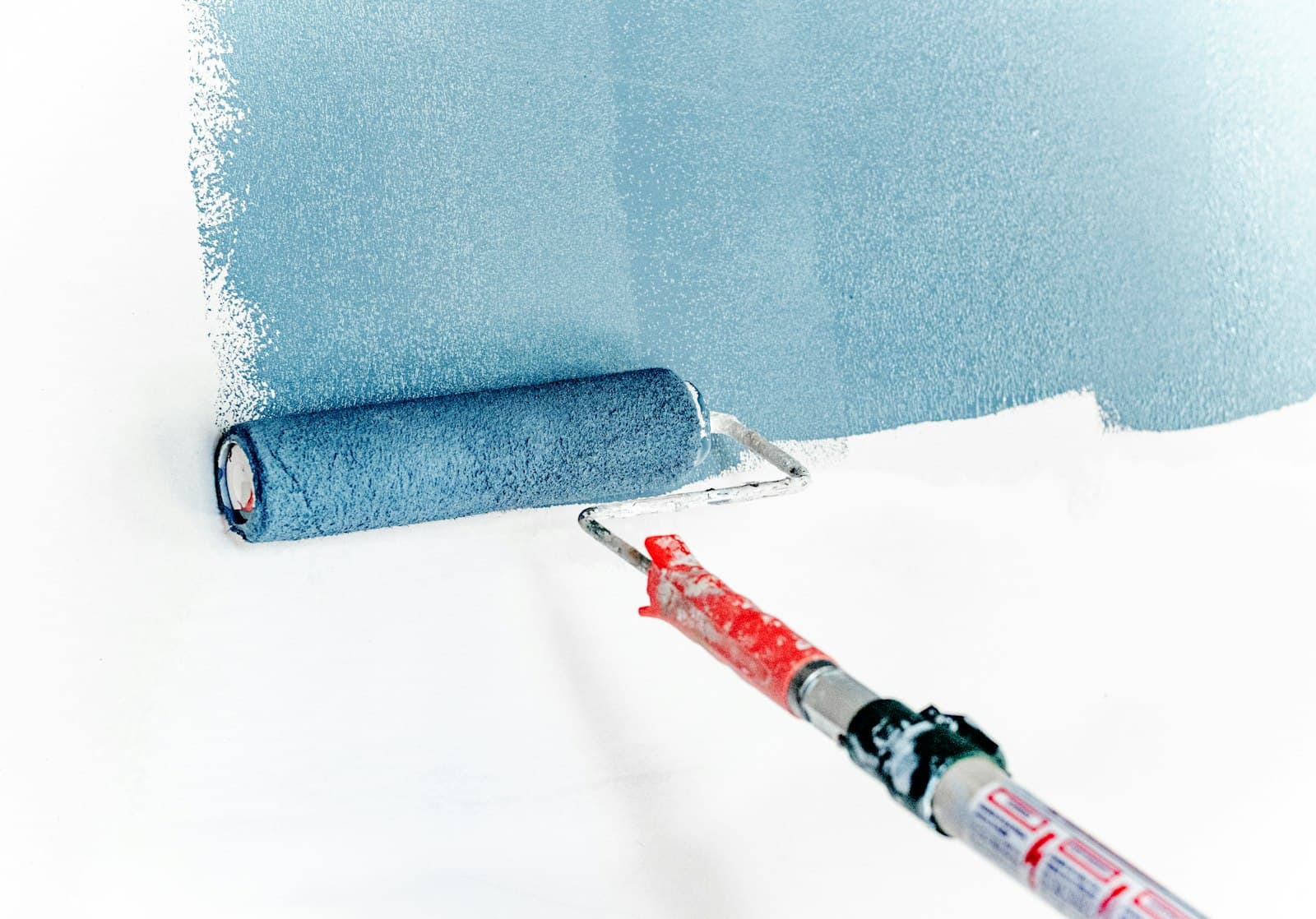 A roller laying fresh blue paint on a wall